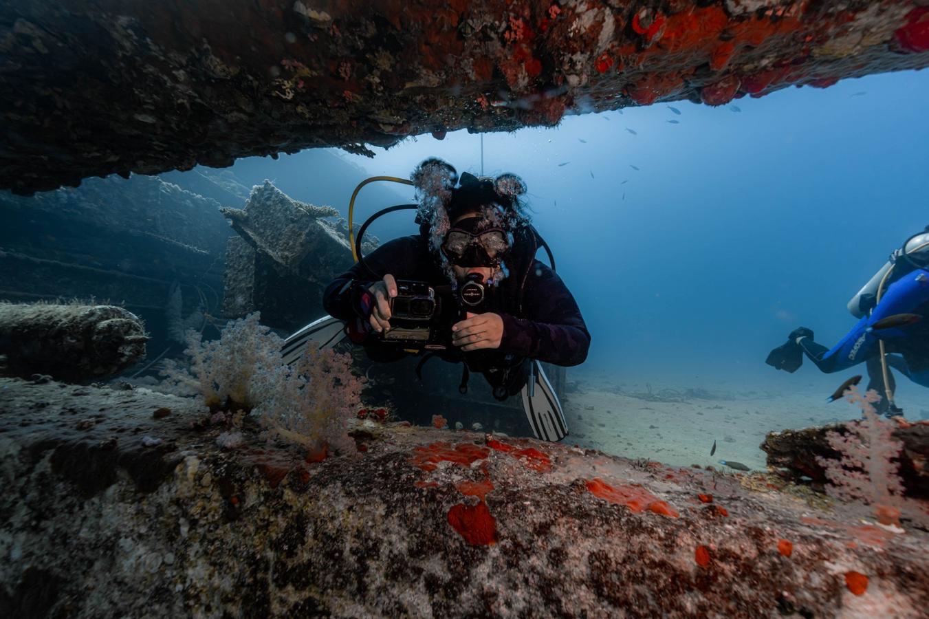 Saudi female scuba diver Bashaer documenting coral reefs underwater in the Red Sea with diving equipment and camera.