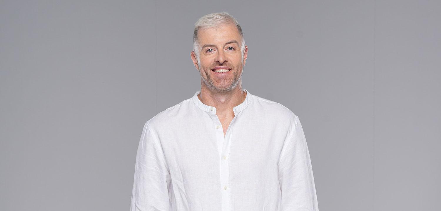 Byron Cooke, host of MBC Loud, in a white shirt and jeans, standing in studio—embodying the international energy of contemporary Saudi broadcasting.