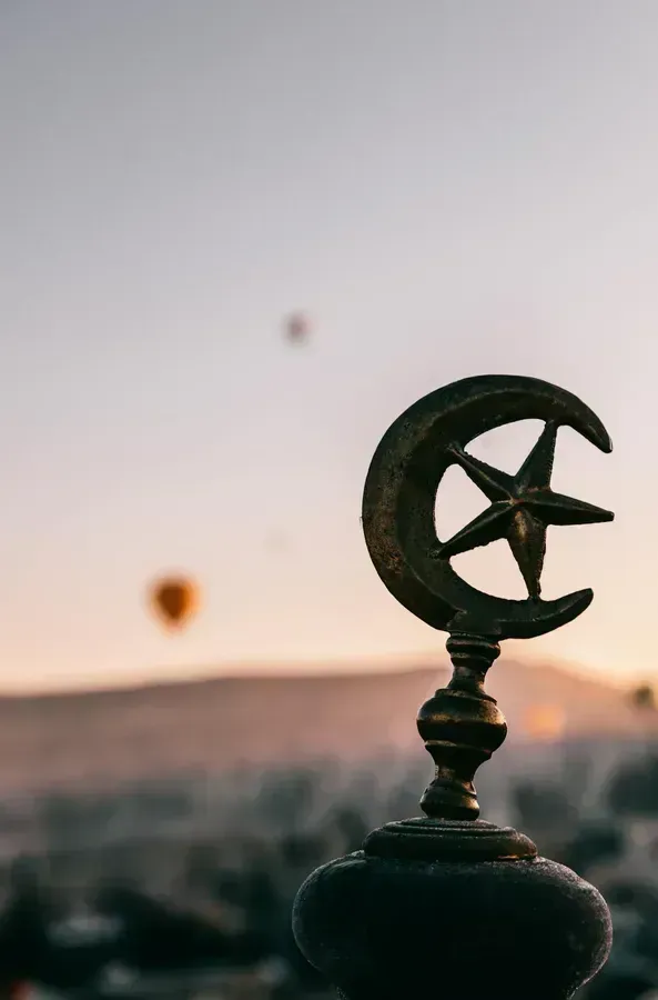A crescent moon and star atop a building, with a hot air balloon in the background, reflecting the intersection of tradition and modernity in the Middle East.