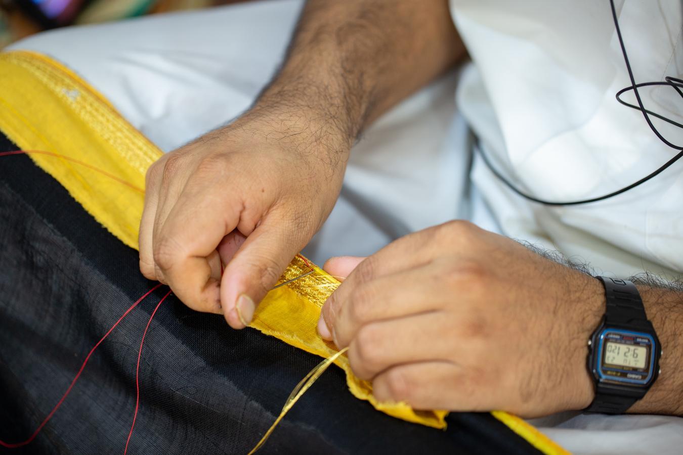 A man threading a bisht, a traditional garment now required for officials, reflecting Saudi cultural identity.