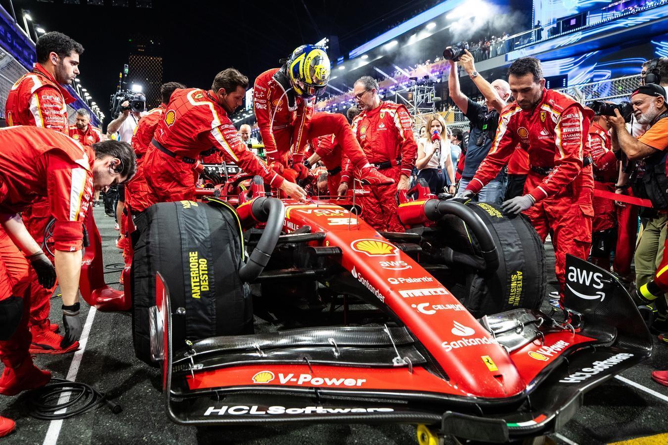 Ferrari Formula One pit crew in red uniforms working on a race car at the Jeddah Corniche Circuit during the Saudi Arabian Grand Prix, surrounded by photographers and bright night lights.