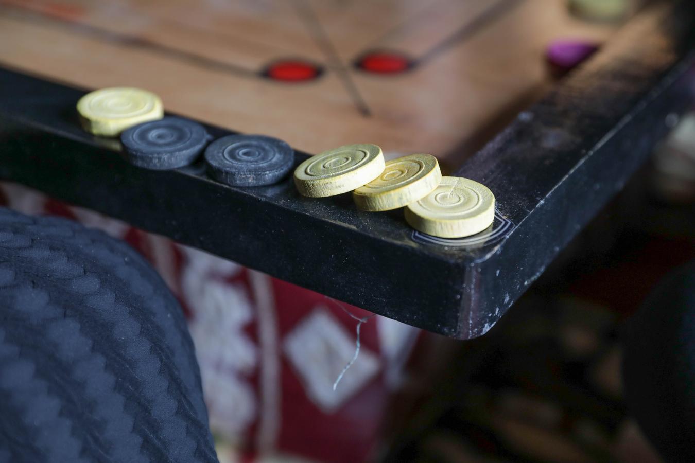 Black and yellow Keram coins line the corner of a wooden board, suggesting a momentary break in a game that blends strategy with subtle skill.