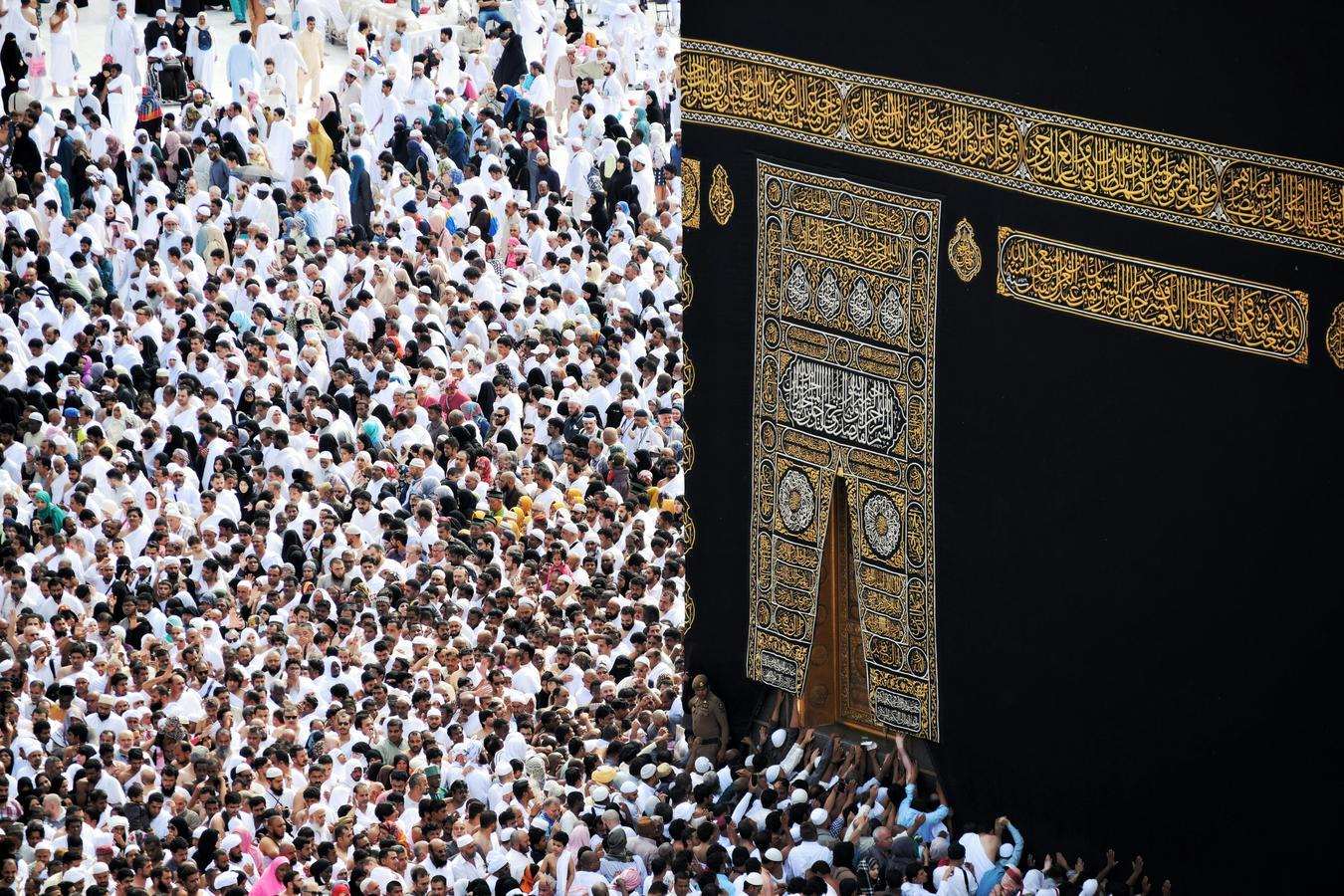 Crowd of pilgrims surrounding the Kaaba in Makkah, touching its golden door, during Hajj or Umrah season.