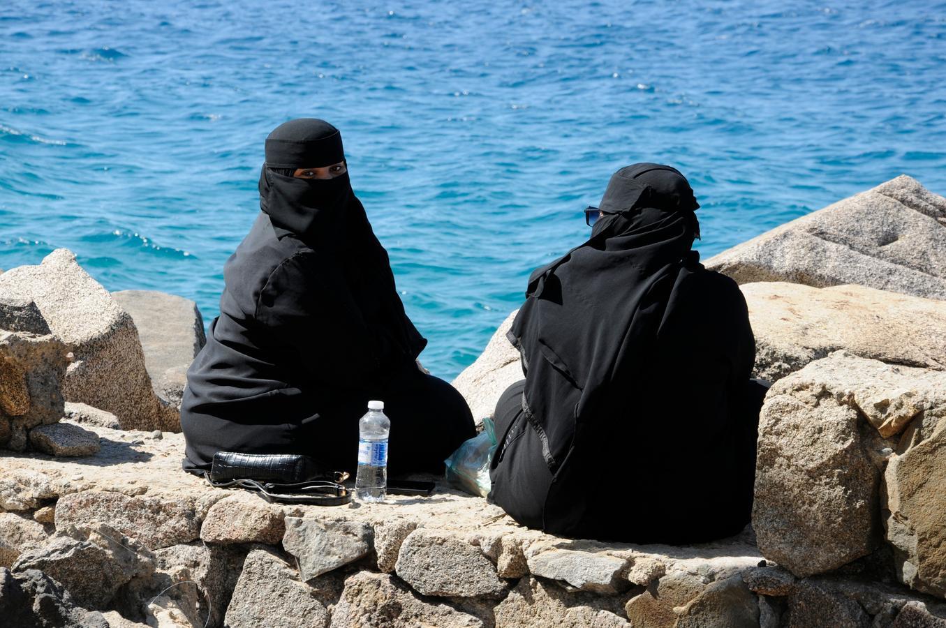 Two Saudi women wearing abayas and niqabs sitting by the Red Sea at Umluj Beach, a rising domestic tourism destination in northwestern Saudi Arabia.