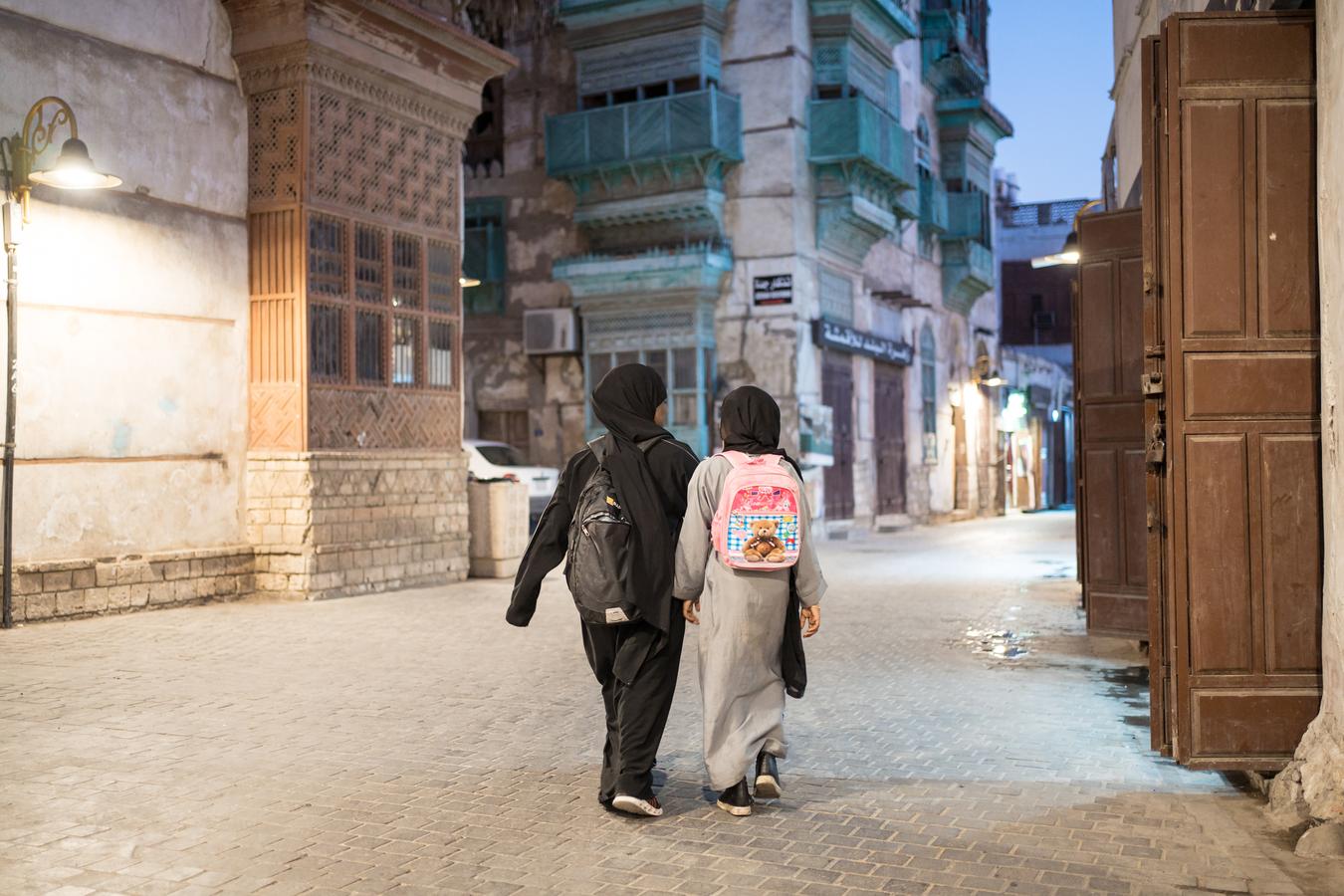 Two Saudi schoolgirls with backpacks walk down a street in the historic Al-Balad district of Jeddah, Saudi Arabia.