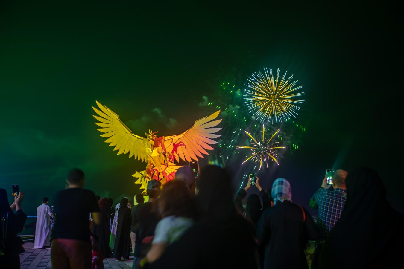 Nighttime festival in Saudi Arabia with fireworks and a sculptural display, where people gather in public space, reflecting the shift toward visible, community-based evening culture.